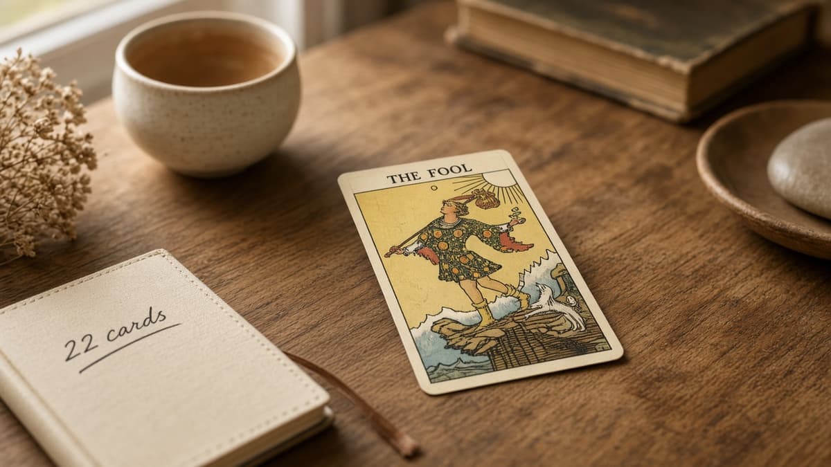 Major Arcana cards still life: one face-up tarot card and a notebook marked 22 cards on a warm wooden desk